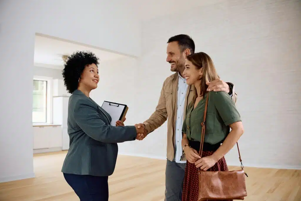 Happy couple and their real estate agent shaking hands in a new house.